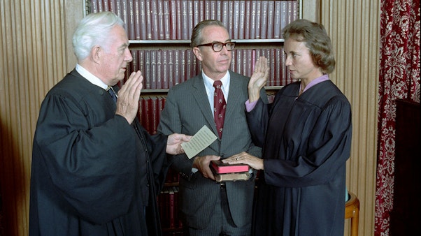 Sandra Day O'Connor being sworn in as Supreme Court Justice by Chief Justice Warren Burger. Her husband John O'Connor looks on at the U.S. Supreme Court. 09/25/1981. Sandra Day O'Connor being sworn in as Supreme Court Justice by Chief Justice Warren Burger with a bookshelf in the background