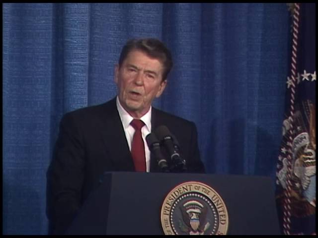 President Ronald Reagan speaking at a podium in front of a blue curtain