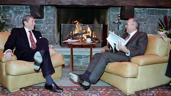 President Reagan and Soviet General Secretary Gorbachev meet in the boathouse during the Geneva Summit in Switzerland. 11/19/1985. Two men in suits sit in tan leather chairs in front of a fireplace