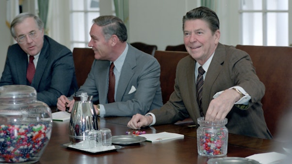 Ronald Reagan in a meeting eating Jelly Beans Giant jar of jelly beans at a table of three men with Ronald Reagan reaching into a smaller jar of jelly beans