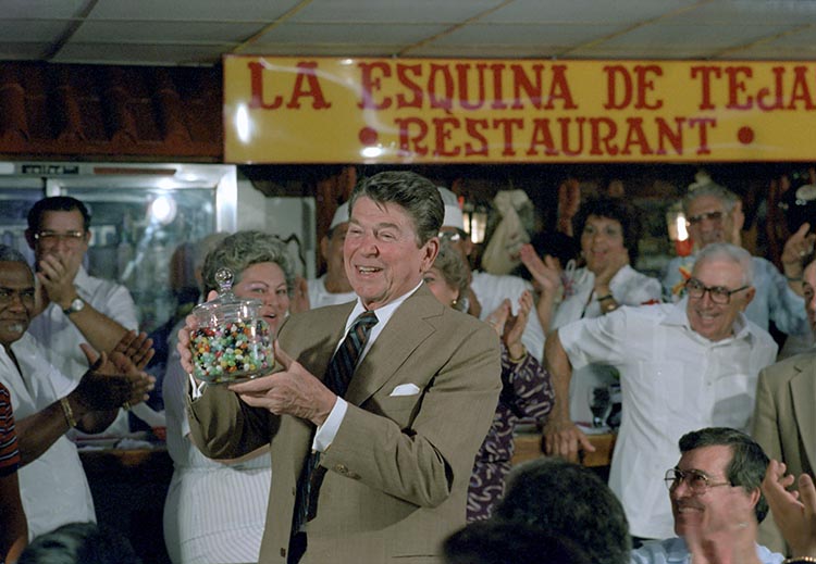 President Reagan in a tan suit holding a jar of jelly beans in front of a crowd of people