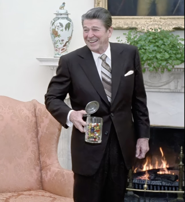 Reagan smiling with jelly bean jar President Ronald Reagan smiling holding a jelly bean jar in the Oval Office in front of a fireplace