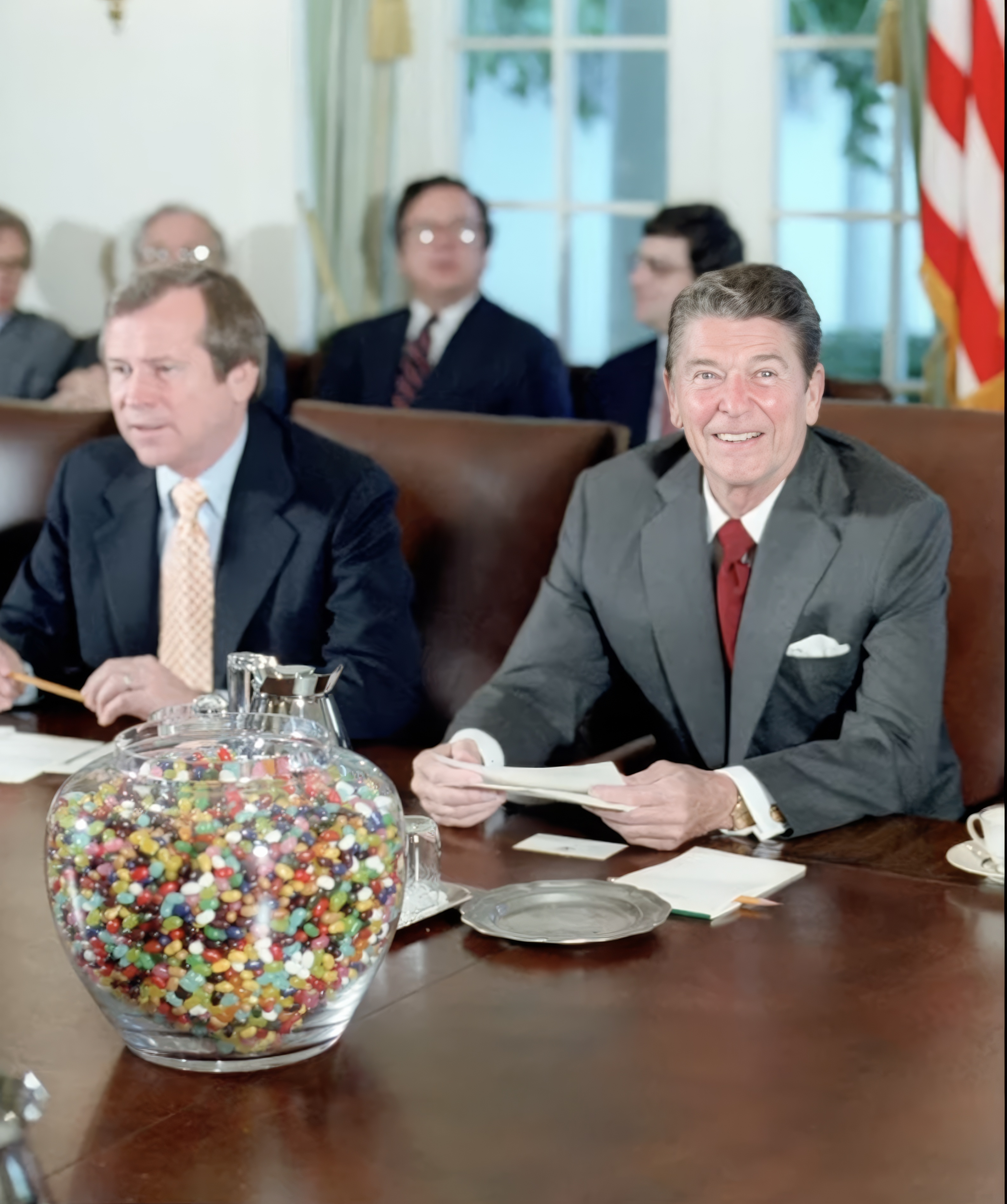 Photo of President Reagan sitting with people at a large brown table with a giant colorful jelly bean jar
