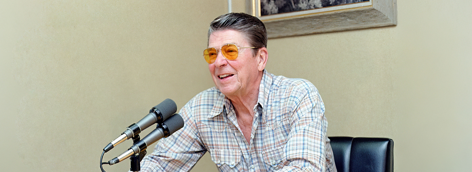 President Reagan sitting behind the desk with microphones