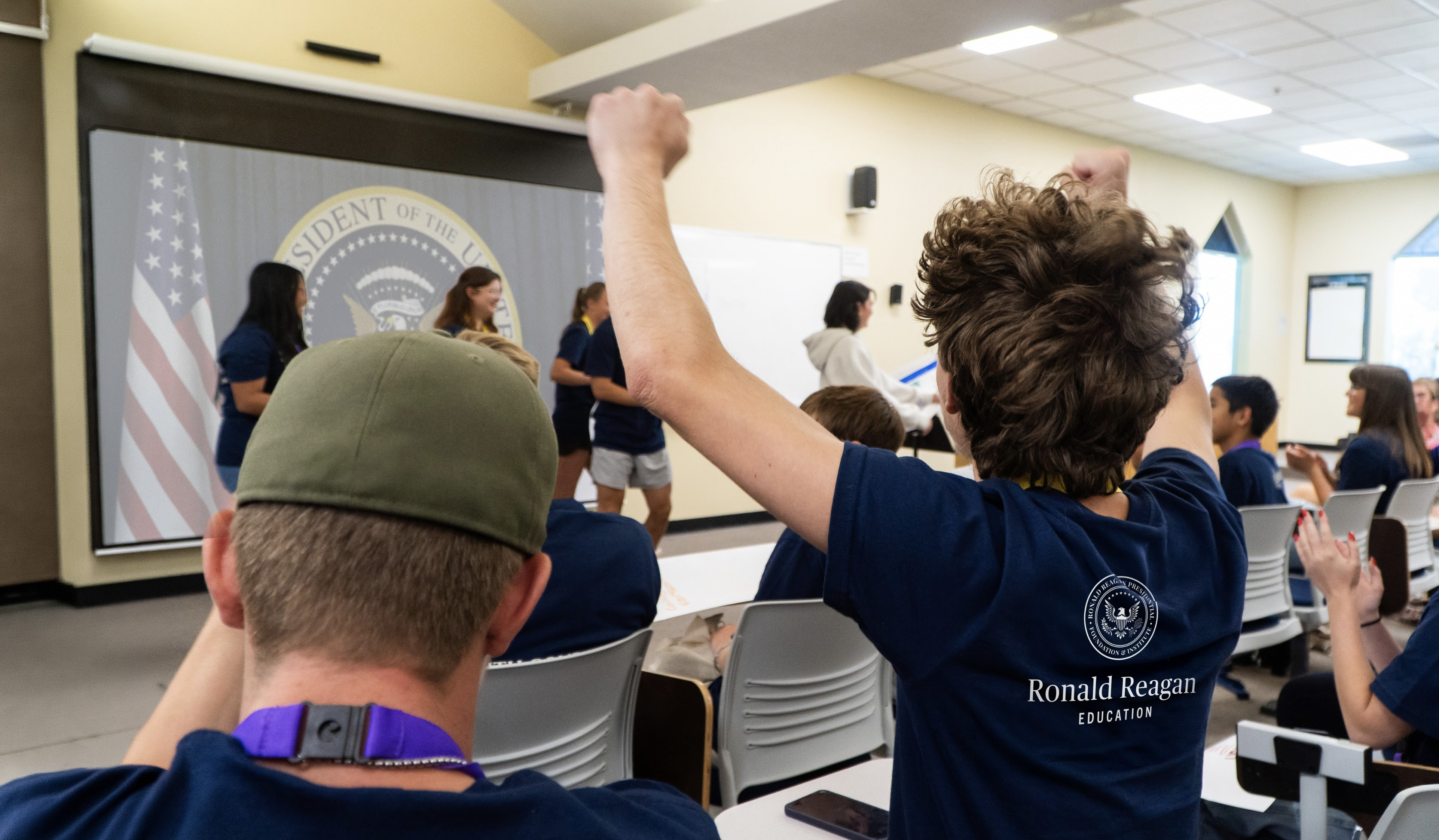 A kid cheering with both fists in the air at his classmates presenting