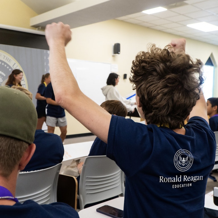A kid cheering with both fists in the air at his classmates presenting